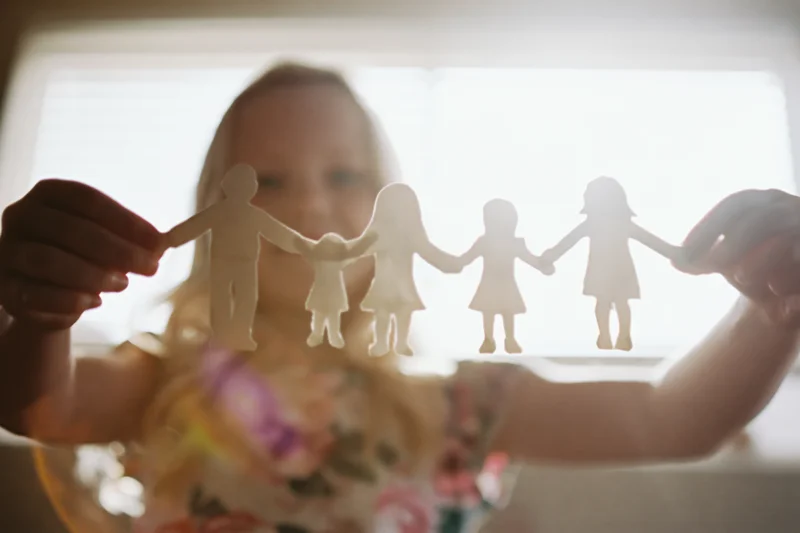 Young blonde girl holding paper cutout family chain against window light