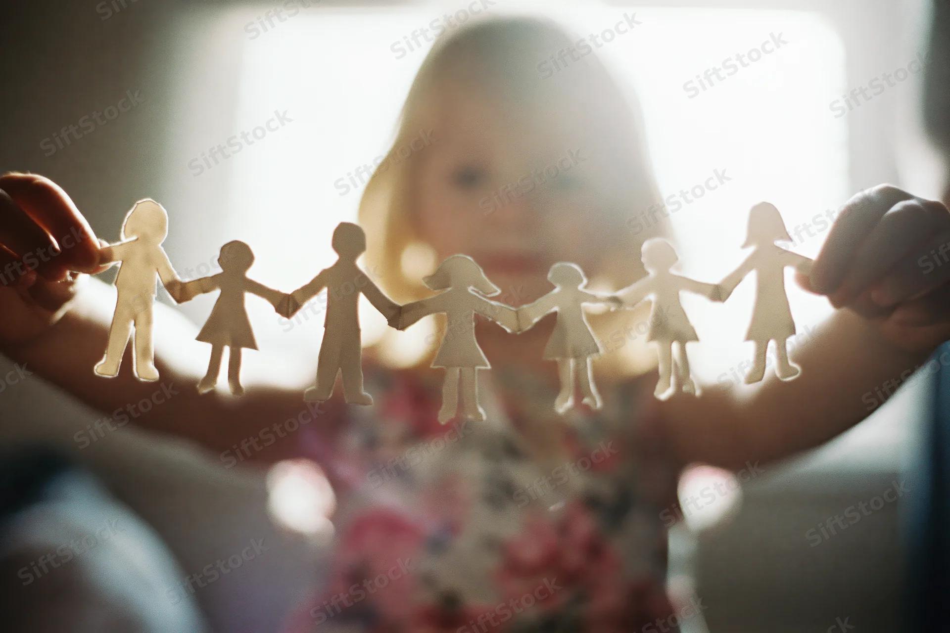 Young blonde girl holding paper cutout family chain in front of window light
