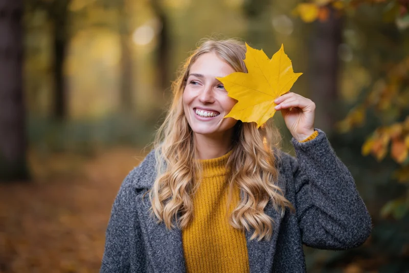 Young blonde woman holding a yellow maple leaf to cover eye