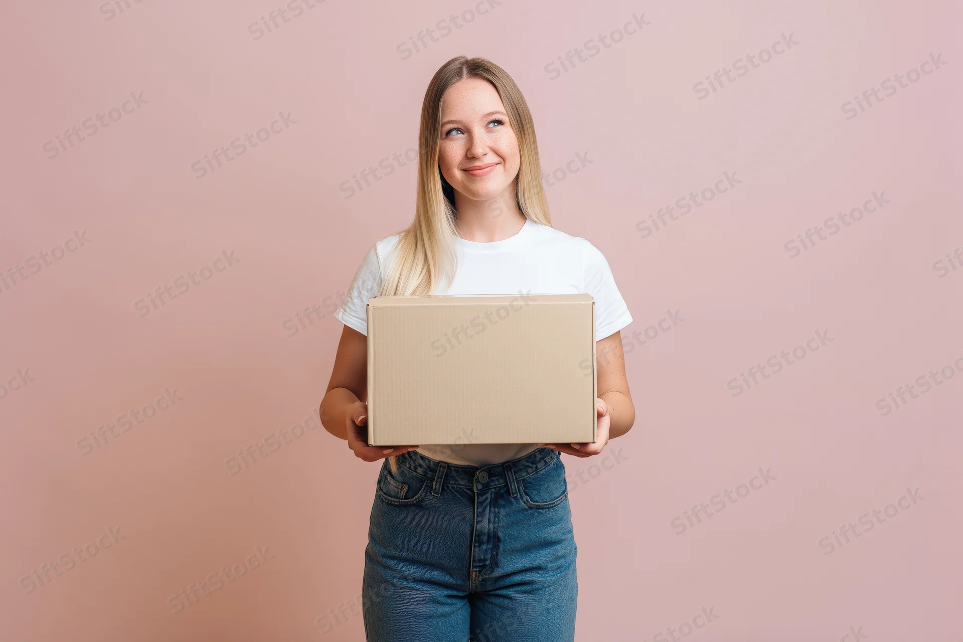 Young blonde woman holding a cardboard box against a pink studio background