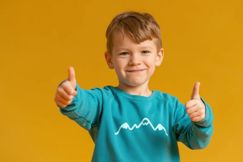 Young boy smiling and giving two thumbs up against yellow background