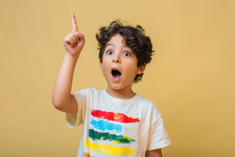Young boy with curly dark hair pointing upward in surprise against yellow background