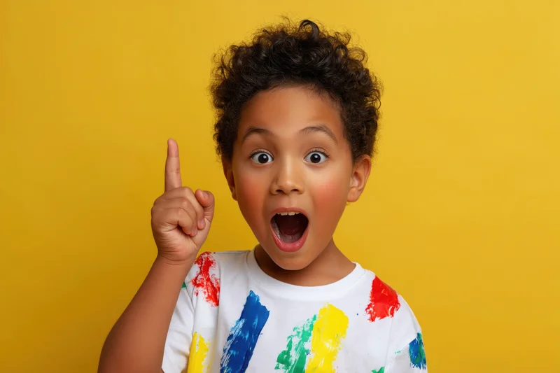 Young boy with curly hair pointing finger upward in surprise against yellow background