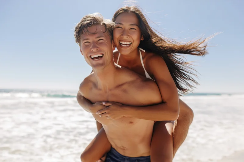 Young couple laughing while piggybacking on a sunny beach