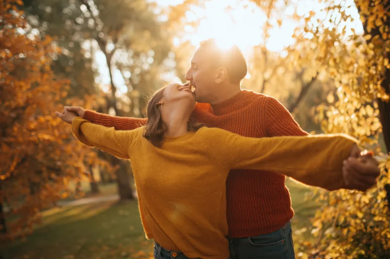 Couple embracing and laughing in an autumn park with arms outstretched