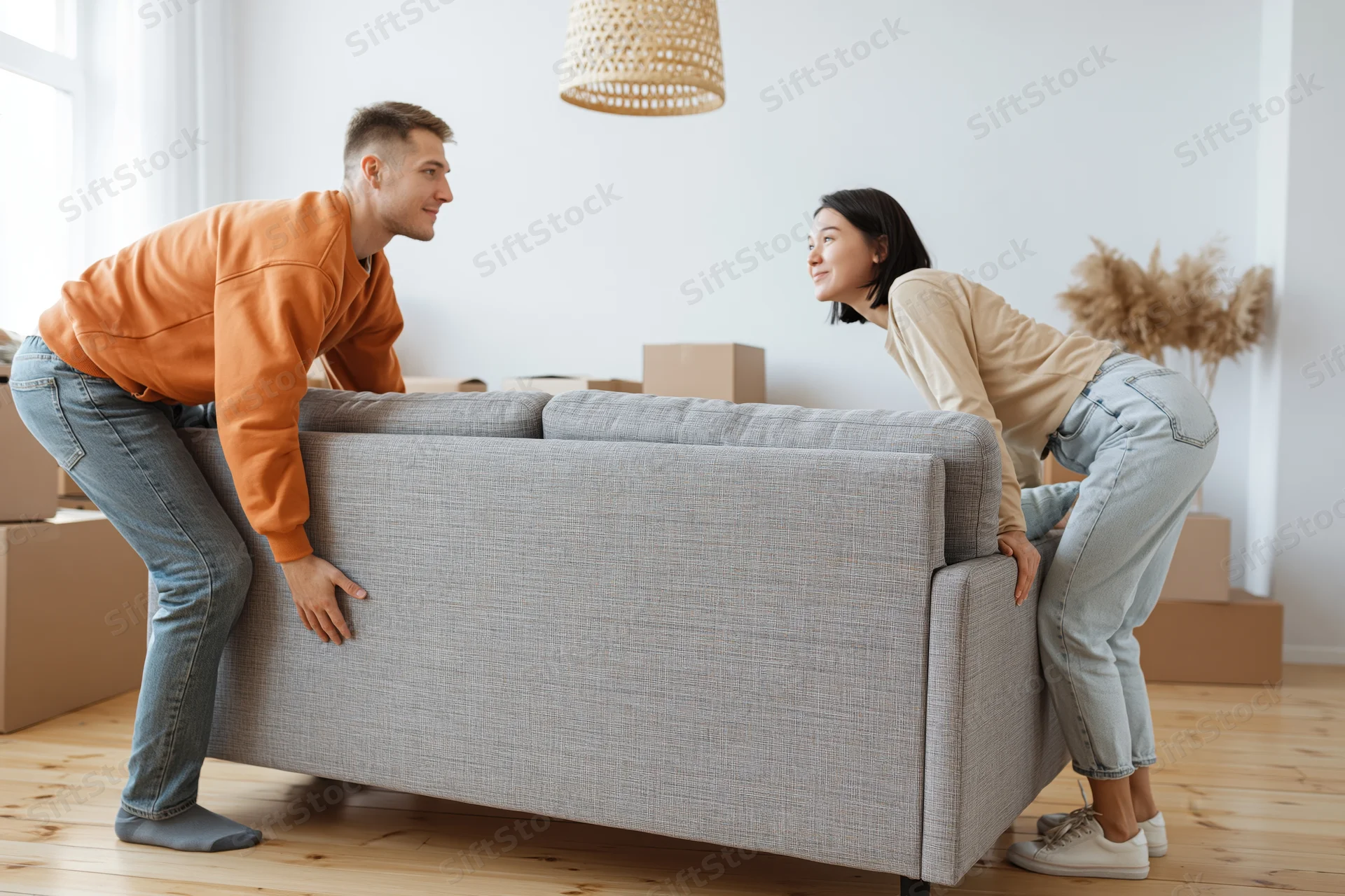 Young couple lifting a gray fabric sofa together in their new apartment