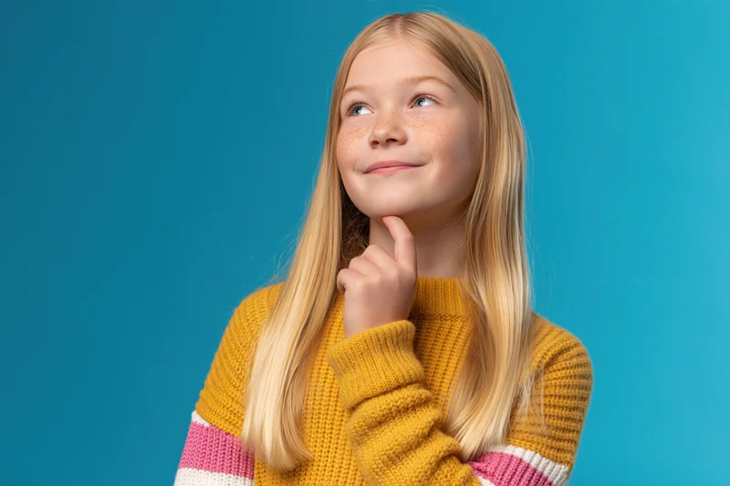 Young blonde girl thinking with finger on chin against blue background