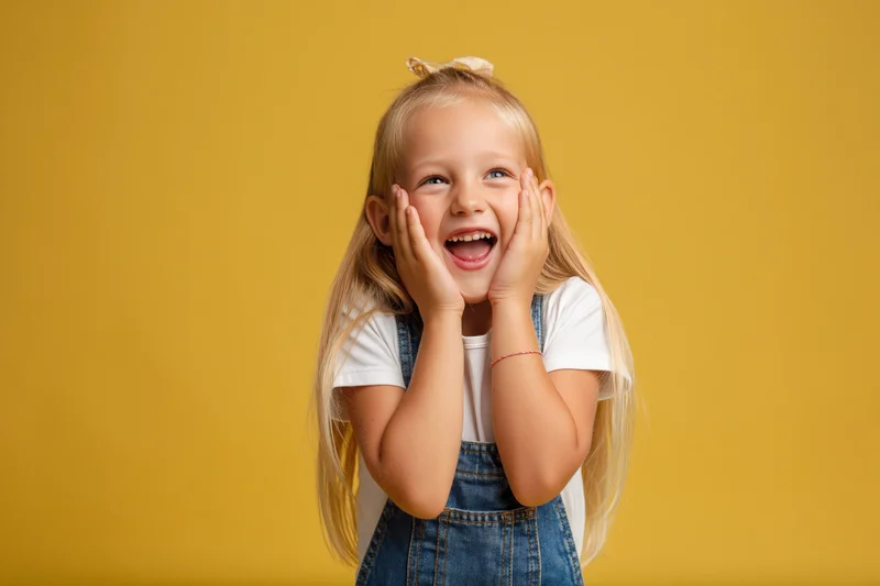 Young girl laughing with hands framing her face against yellow background