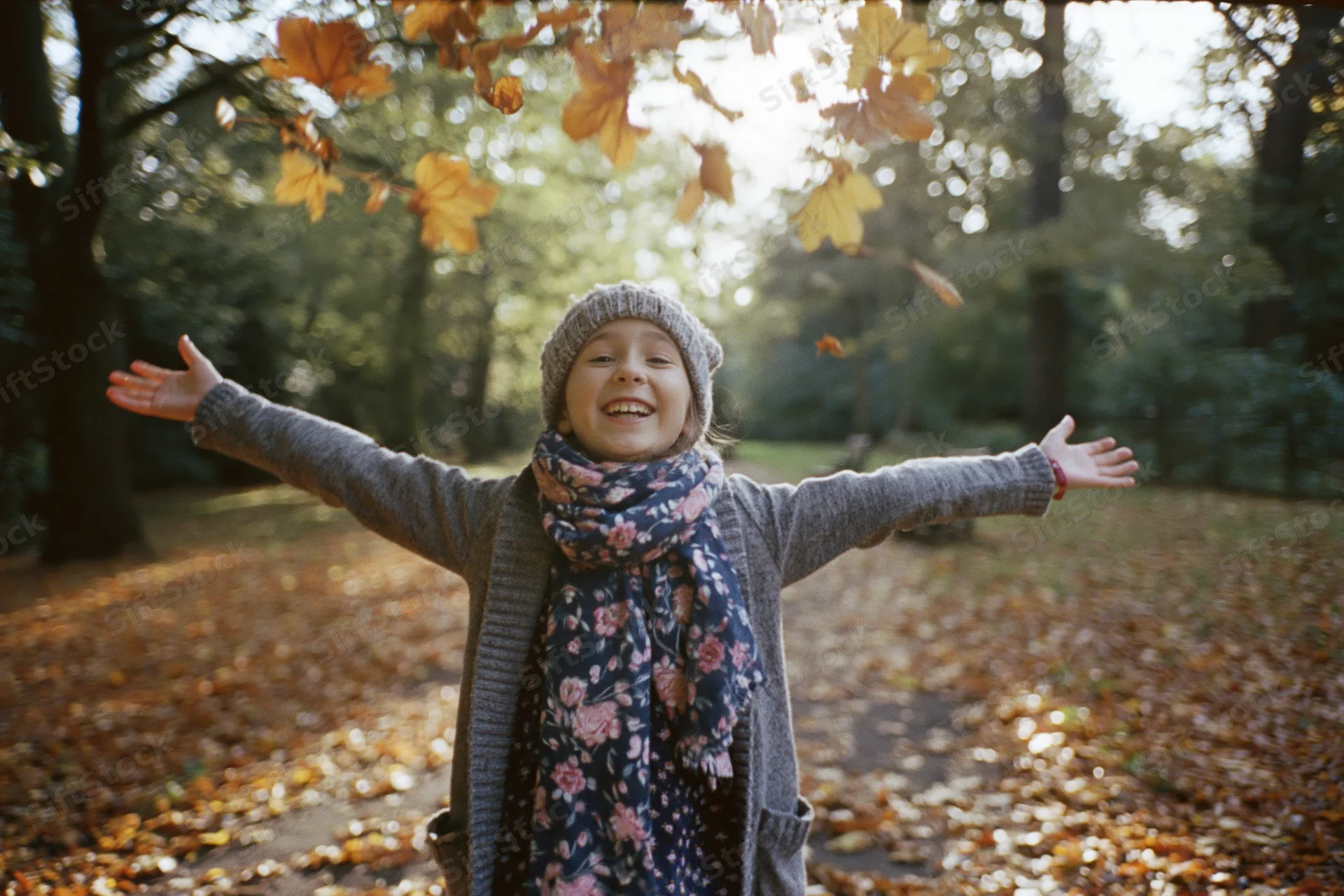 Young girl laughing with arms outstretched in autumn forest surrounded by falling leaves