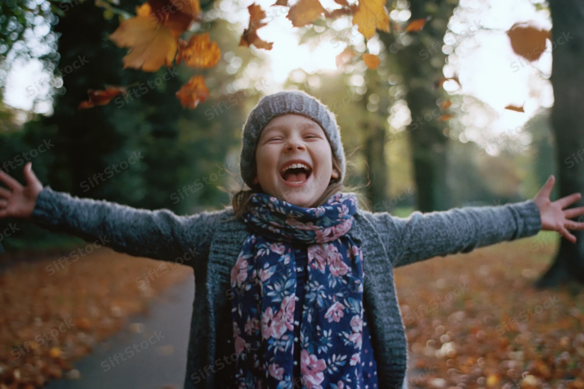 Young girl laughing with arms outstretched in autumn park surrounded by falling leaves