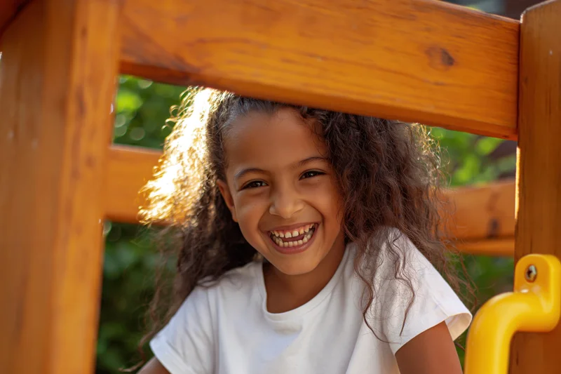 Girl smiling widely through wooden playground structure outdoors
