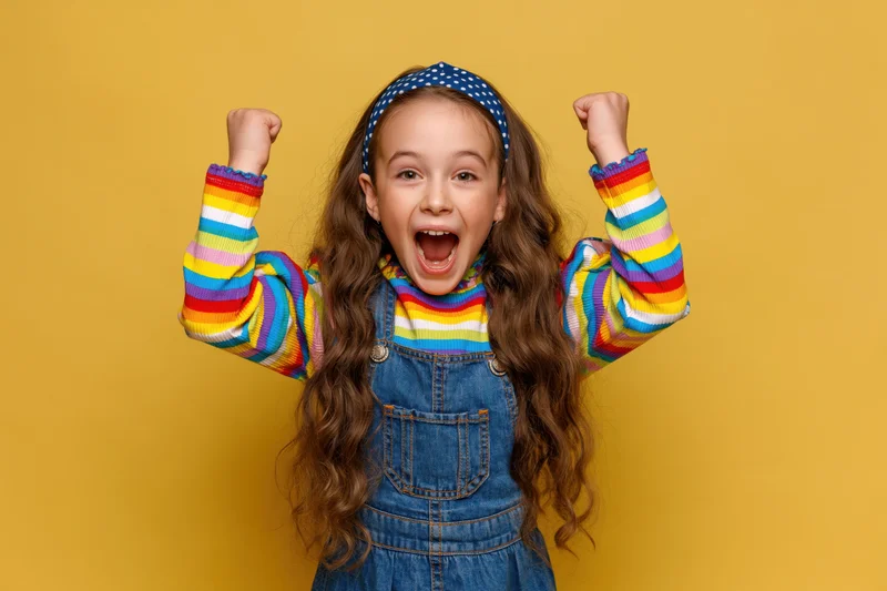 Young girl cheering with raised fists against yellow background