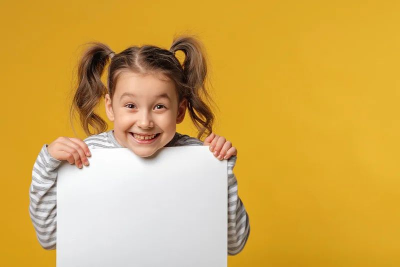 Young girl smiling and peeking over a blank white sign against yellow background