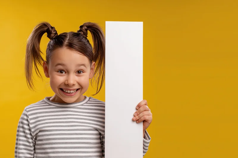 Young girl smiling and peeking from behind a white sign against yellow background