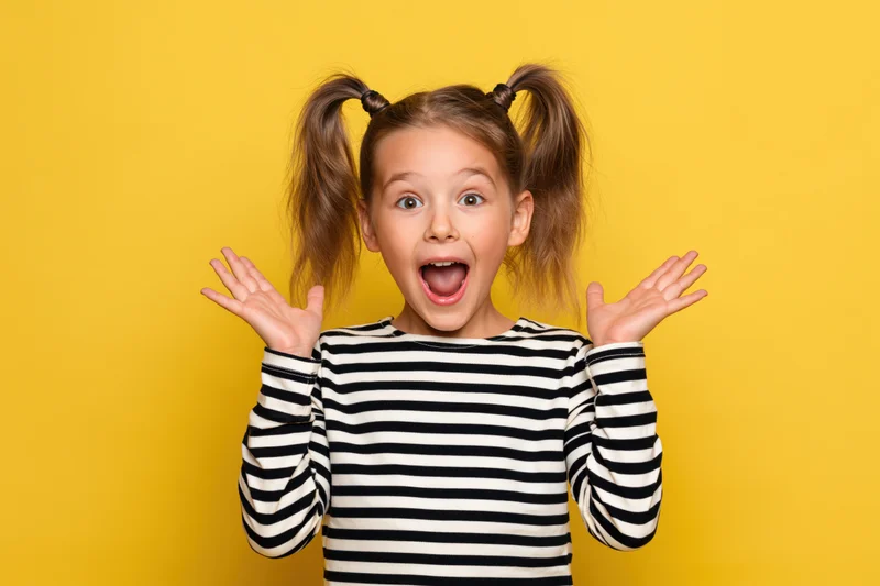 Young girl with wide eyes and open mouth, hands raised, wearing striped shirt against yellow background