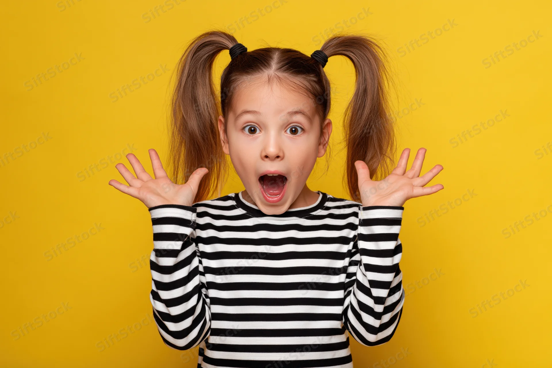 Young girl with high ponytails making surprised expression with hands raised against yellow background