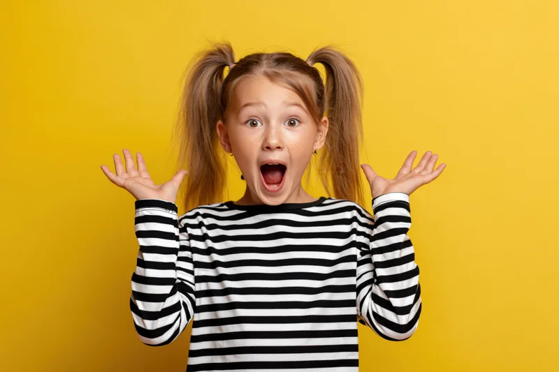Young girl with high ponytails showing surprised expression with hands raised against yellow background