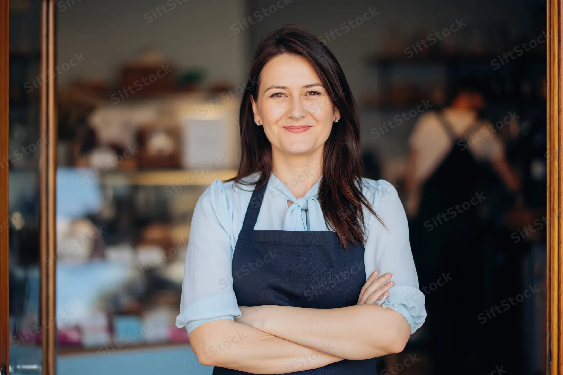 Woman cafe owner standing at bakery doorway with arms crossed smiling