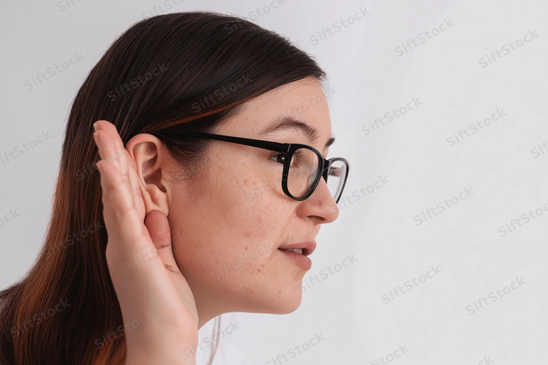 Woman cupping hand behind ear while wearing glasses in profile view against white background