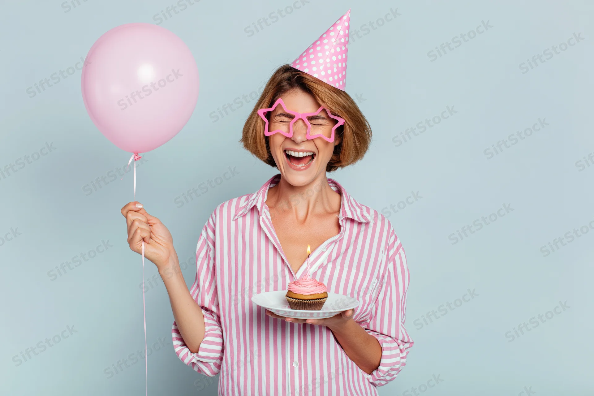 Woman smiling with eyes closed holding cupcake and balloon at birthday party