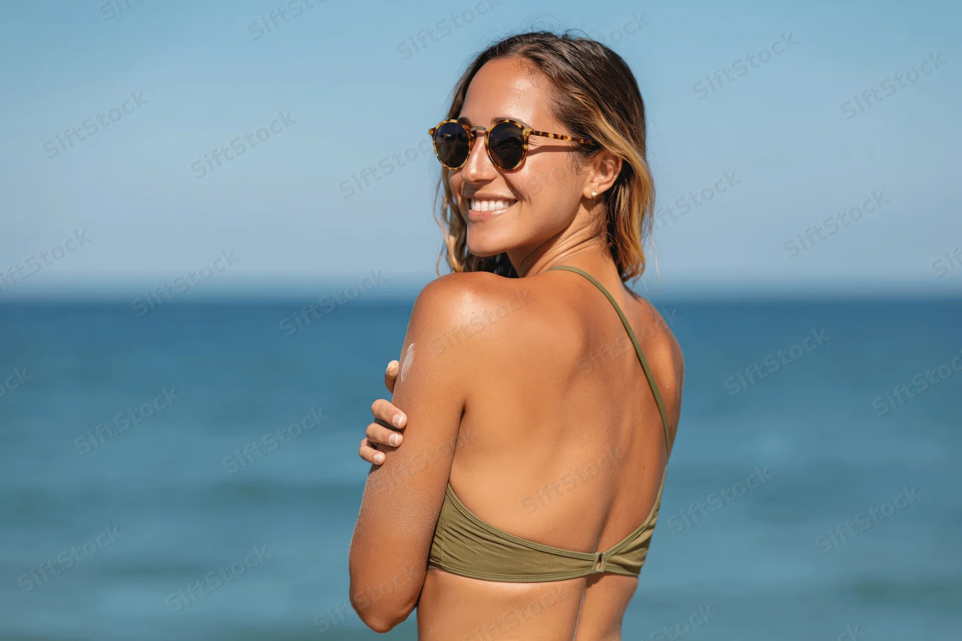 Woman in olive bikini smiling over shoulder at beach with ocean behind