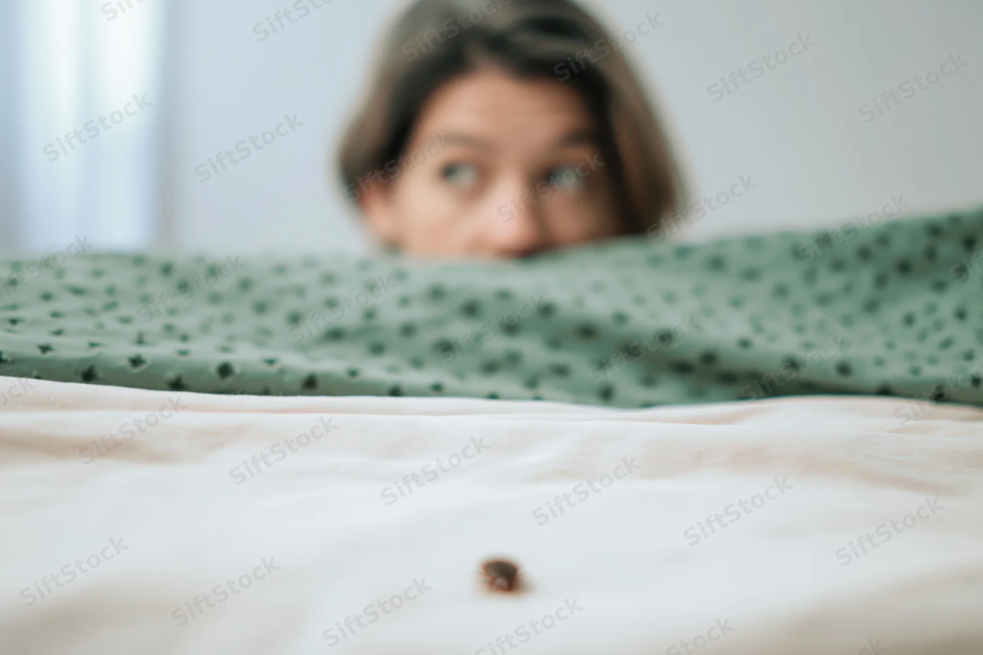 Woman peeking over blanket at bug on bed