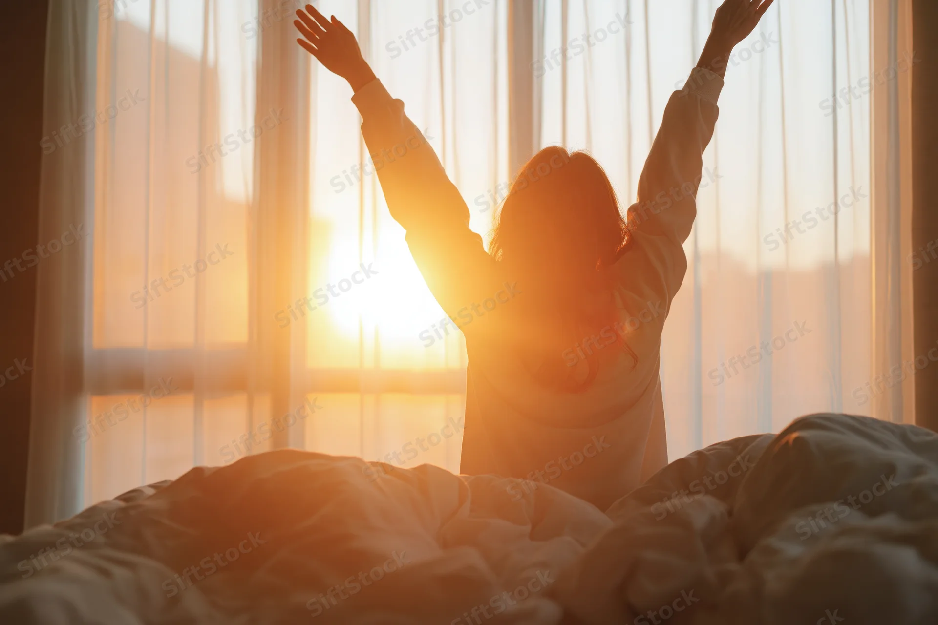 Woman stretching arms overhead in bed at sunrise