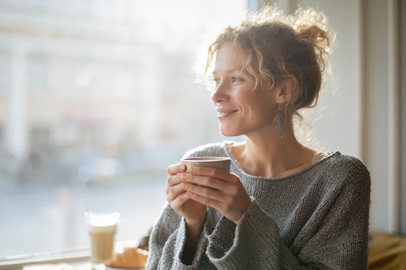 Woman smiling while holding coffee cup by window in cafe