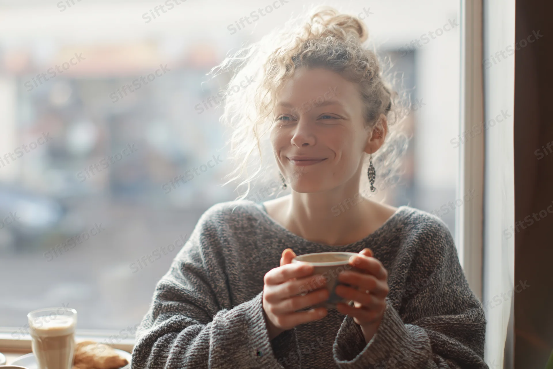 Young woman smiling while holding a coffee cup at a cafe window