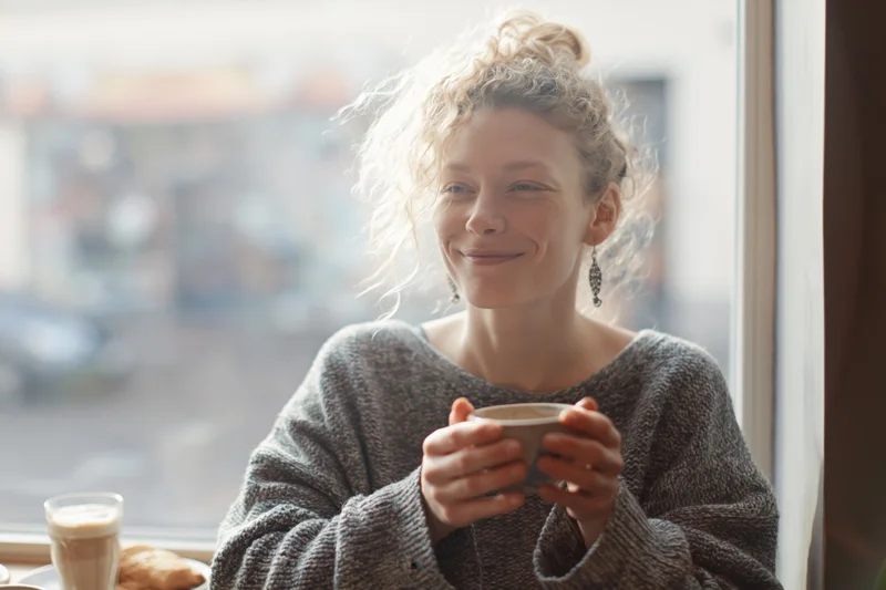 Young woman smiling while holding a coffee cup at a cafe window
