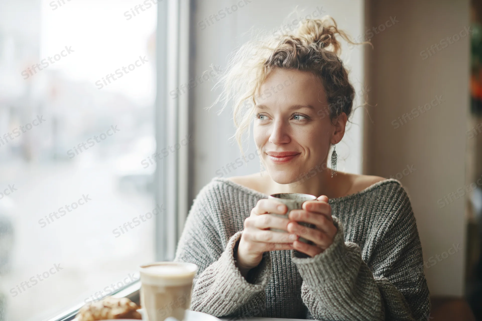 Woman smiling while holding a coffee mug at a cafe window