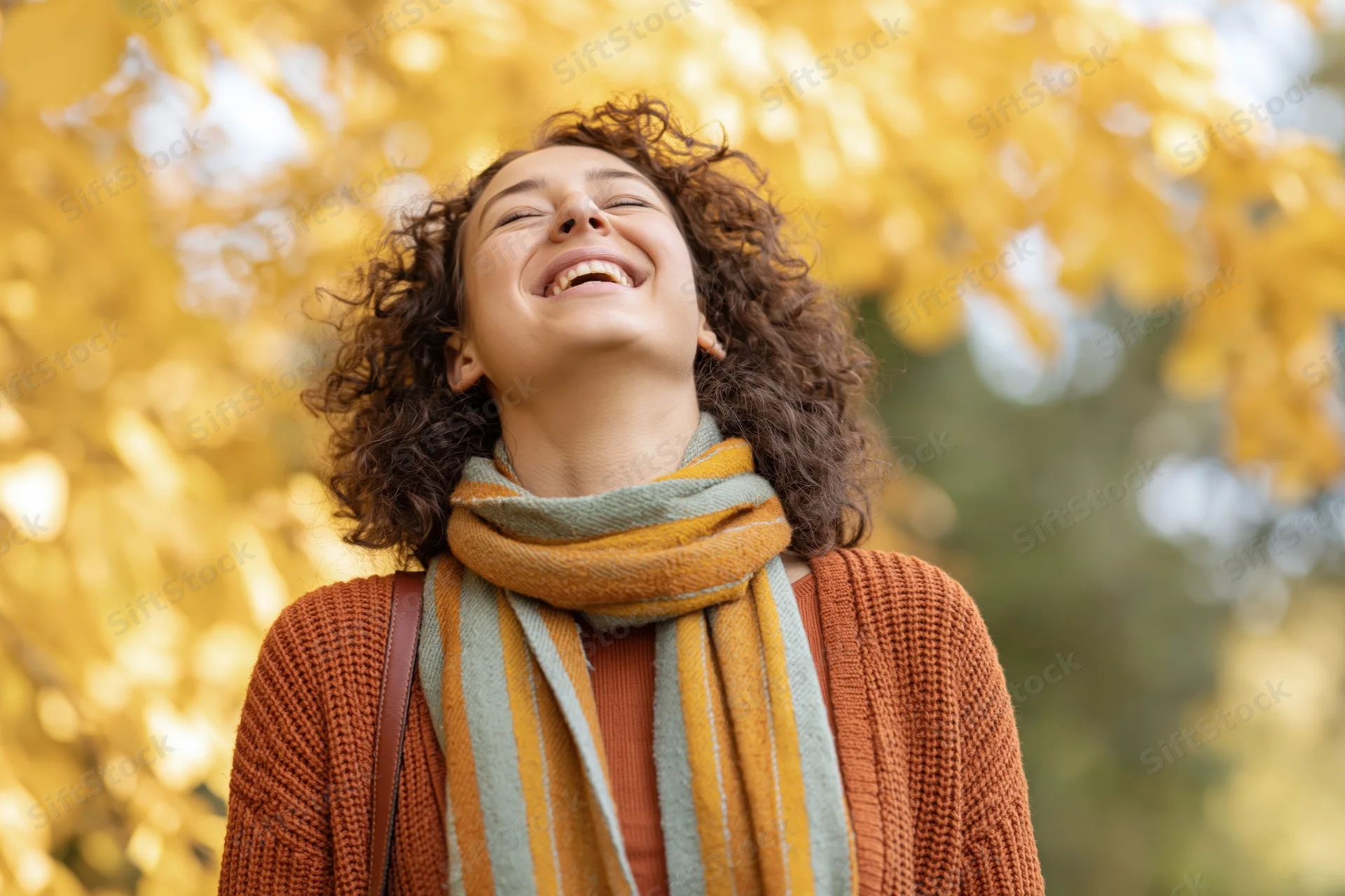Woman laughing with head tilted up in autumn park surrounded by yellow foliage