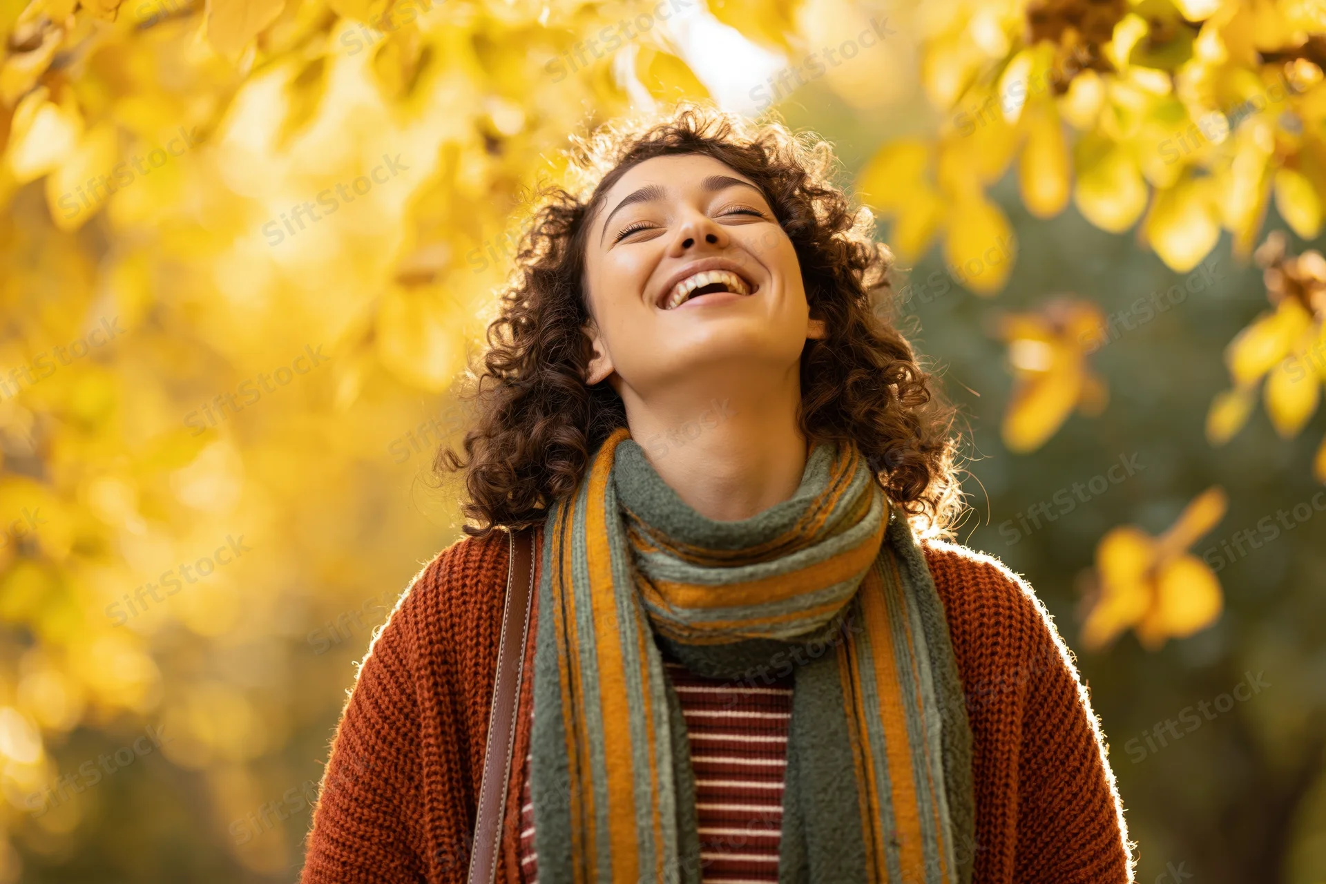 Young woman laughing with head tilted back under golden autumn leaves