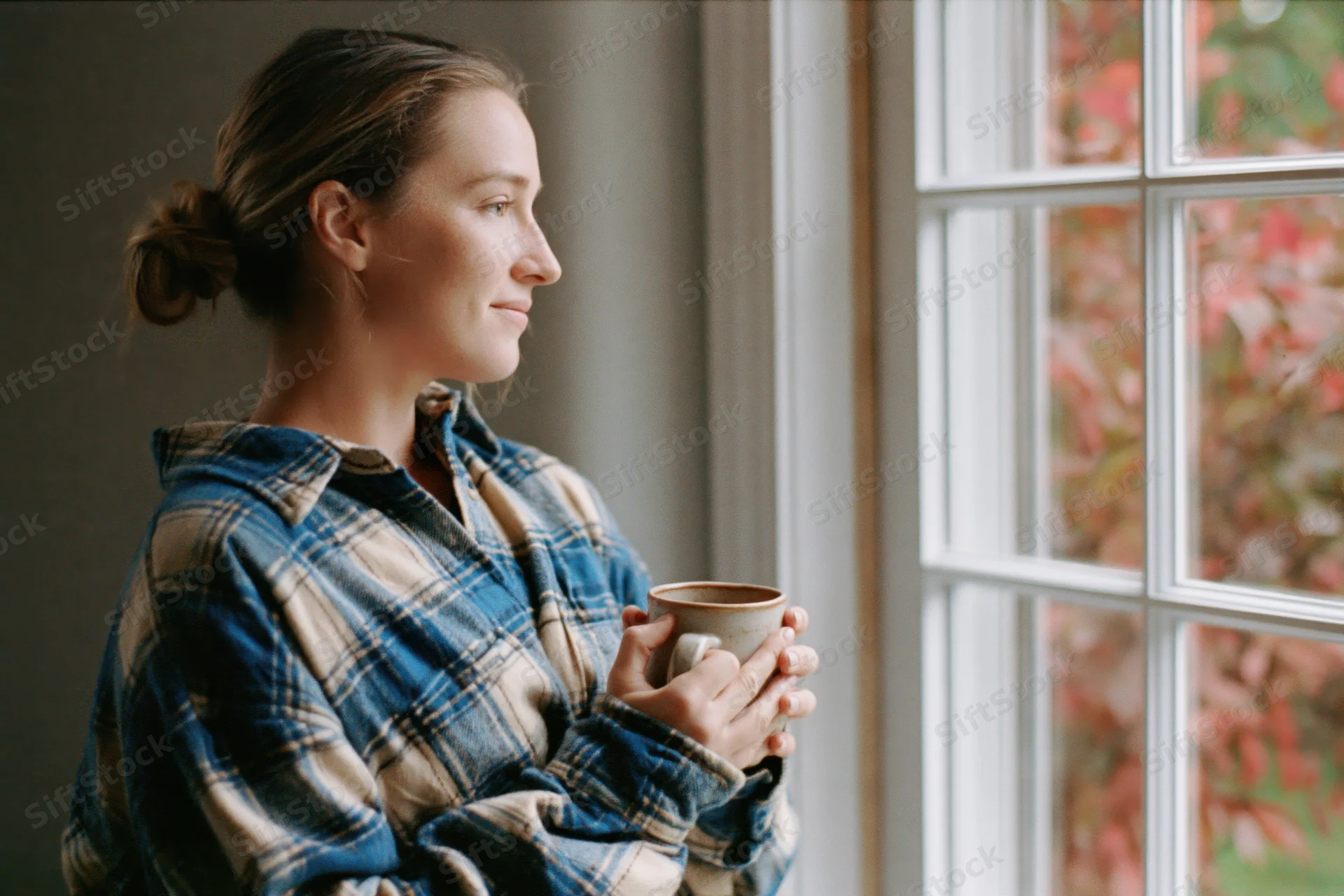 Woman holding mug by window looking at autumn foliage