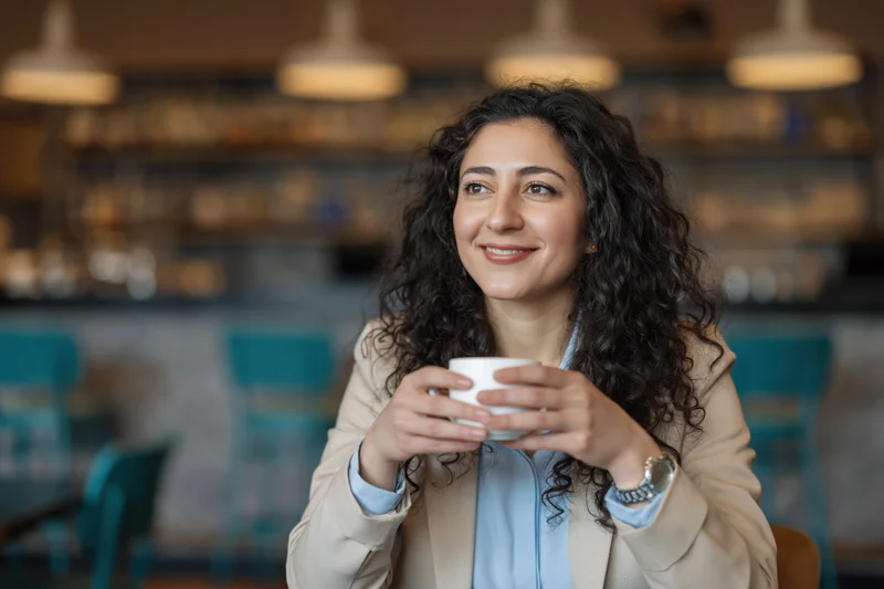 Woman holding a white coffee cup in a cafe interior smiling