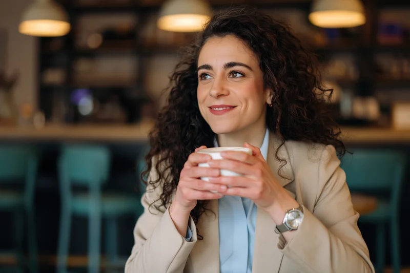 Woman holding a white coffee cup in a cafe interior, smiling and looking away