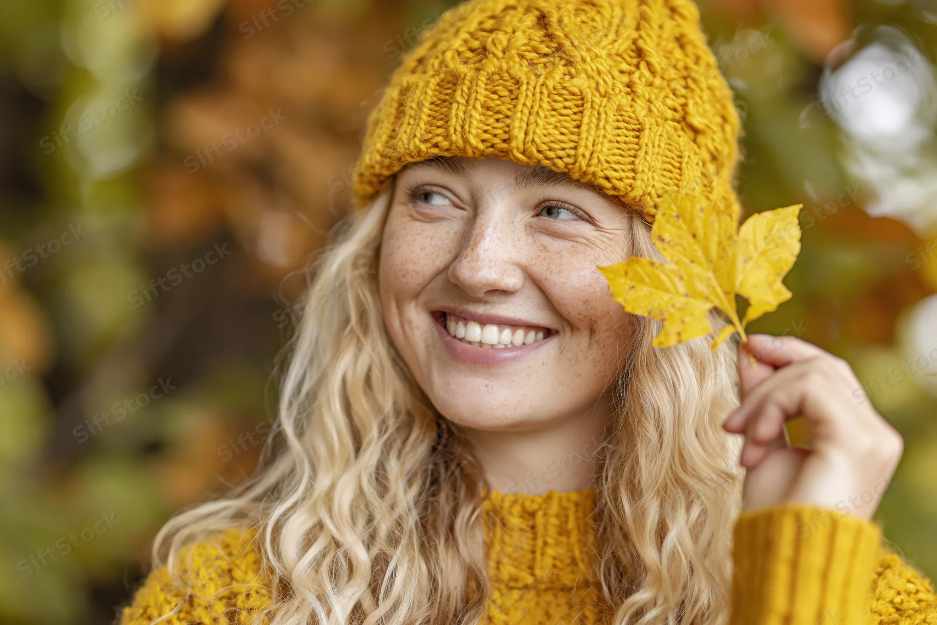 Young woman smiling while holding a yellow leaf outdoors in autumn