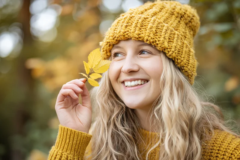 Young woman smiling while holding a yellow leaf in autumn forest