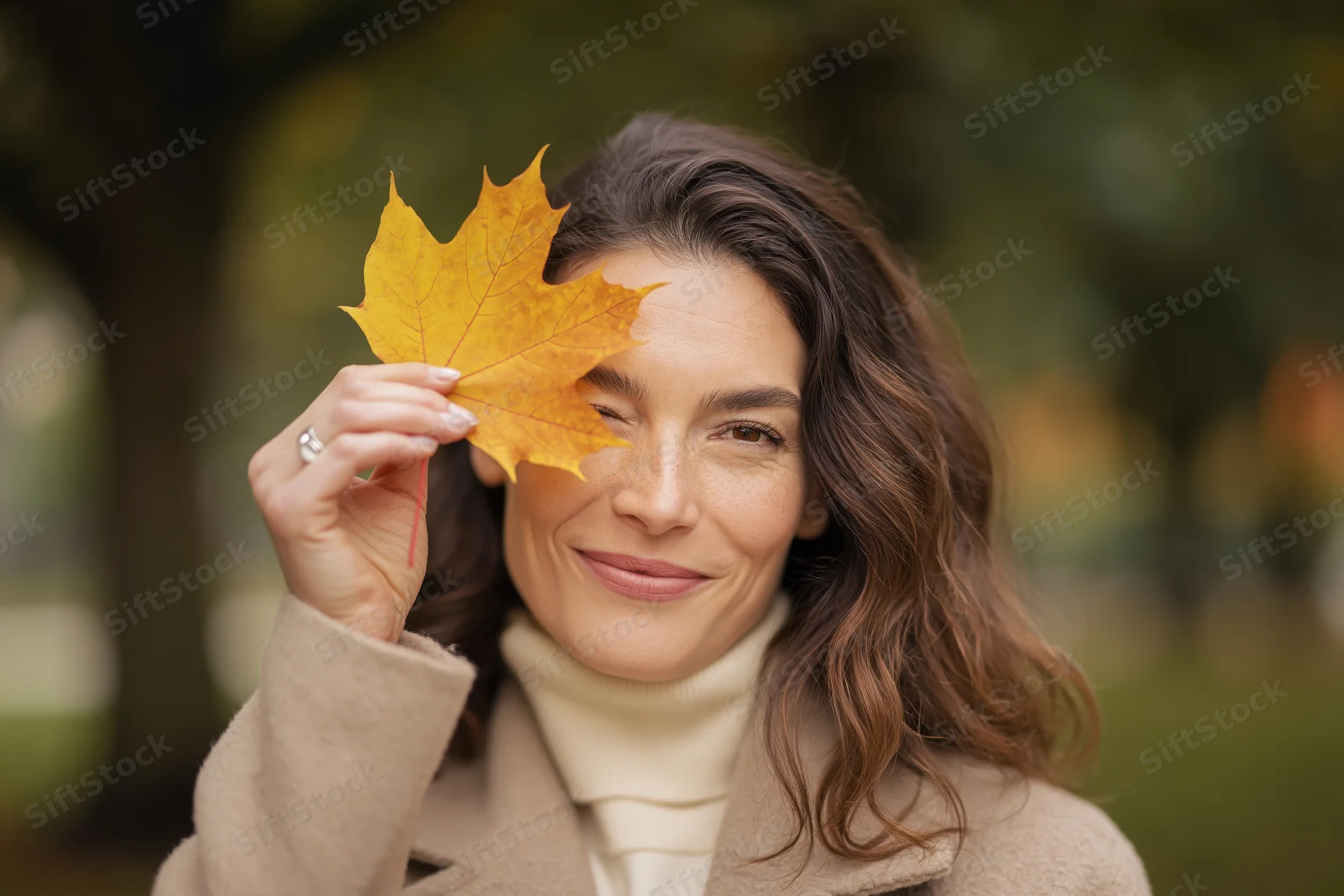 Woman holding a yellow maple leaf over her eye in a park during autumn