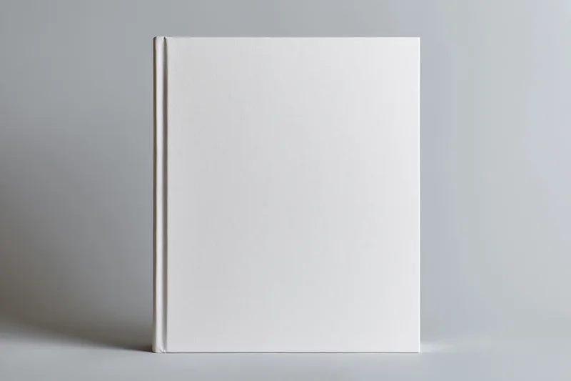 Blank white hardcover book standing upright on a neutral gray surface