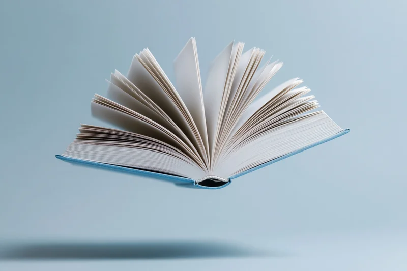 Open hardcover book floating mid-air against a light blue background