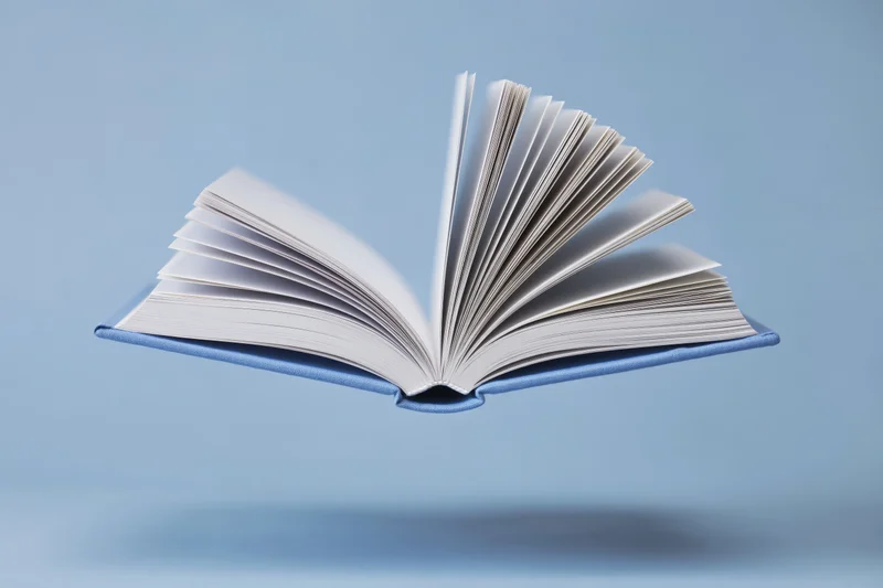 Open hardcover book floating mid-air against a blue background
