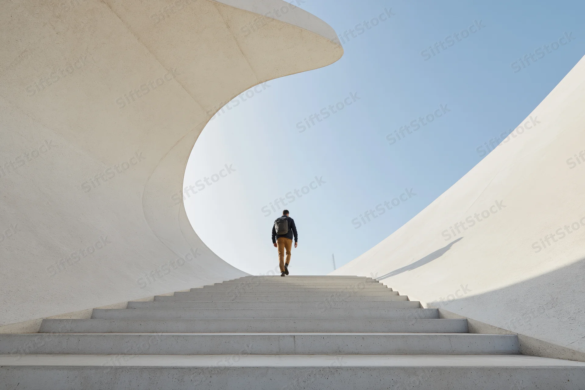 Man with backpack climbing wide concrete stairs under curved white structure outdoors
