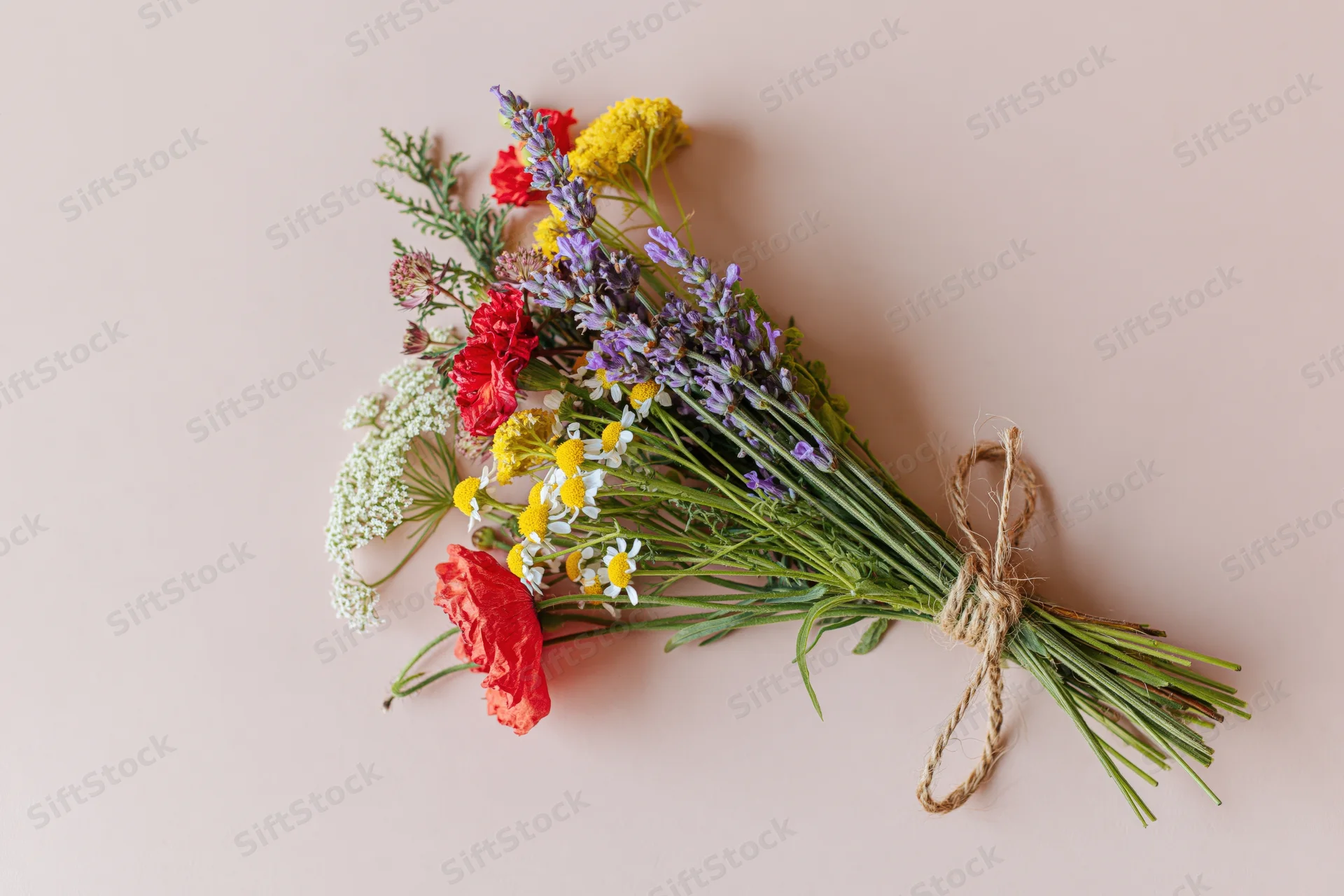 Loose wildflower bouquet tied with twine lying flat on pale blush pink surface