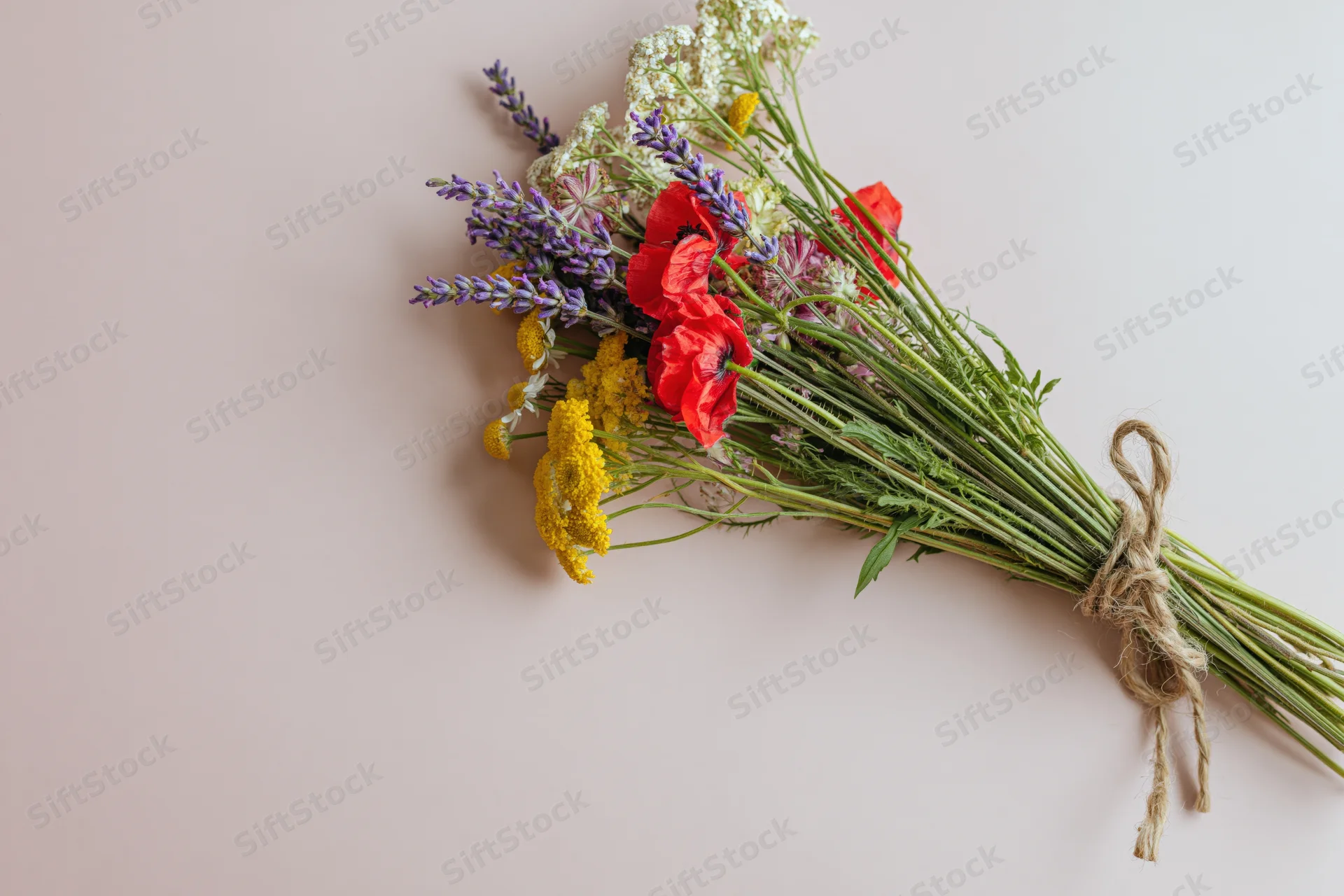 Loose wildflower bouquet tied with twine lying flat on pale pink surface