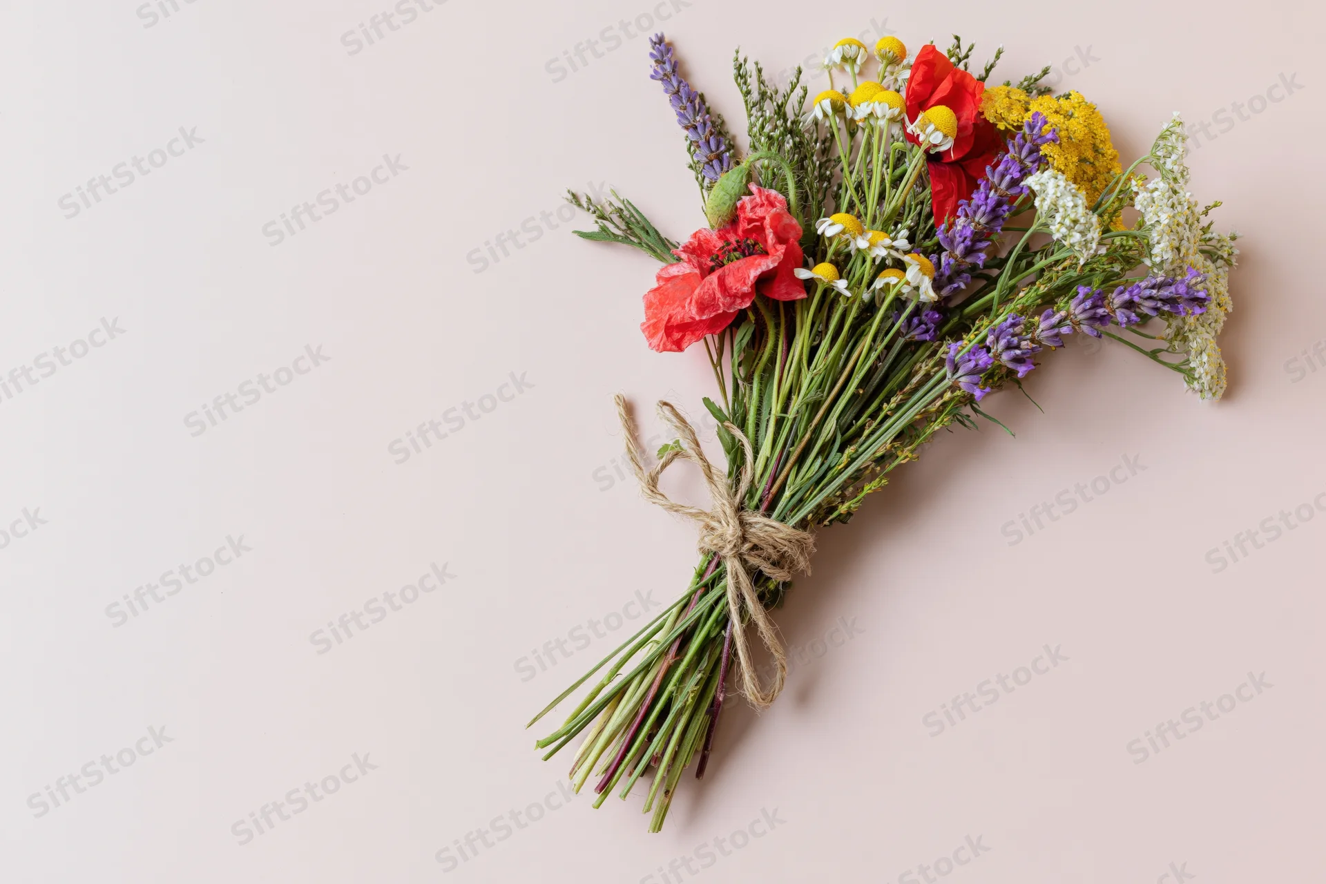 Loose wildflower bouquet tied with twine lying flat on pale pink surface
