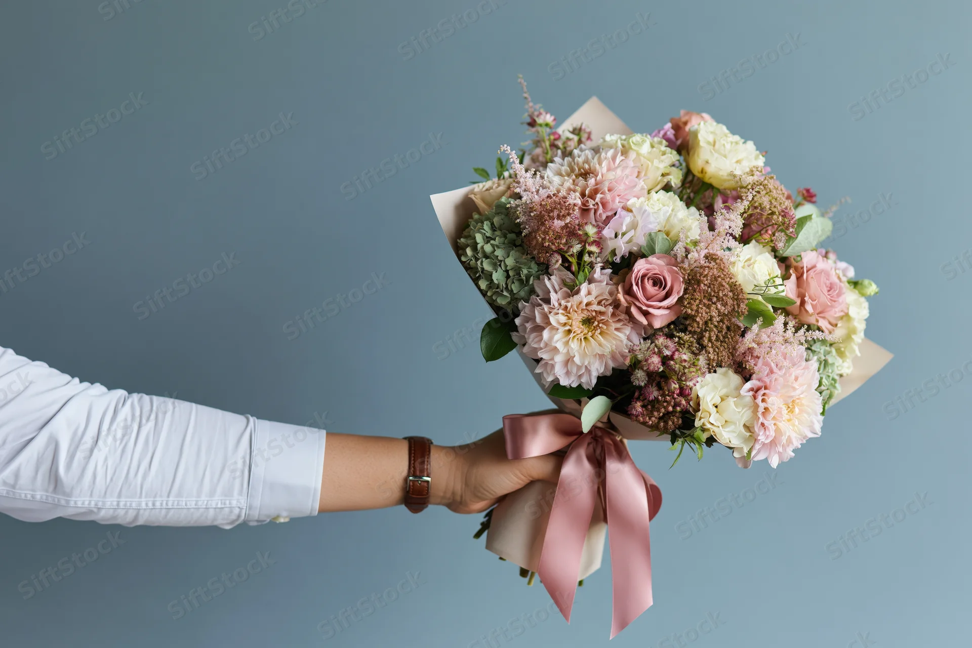 Woman's arm holding a wrapped bouquet of pink and white flowers against a blue background