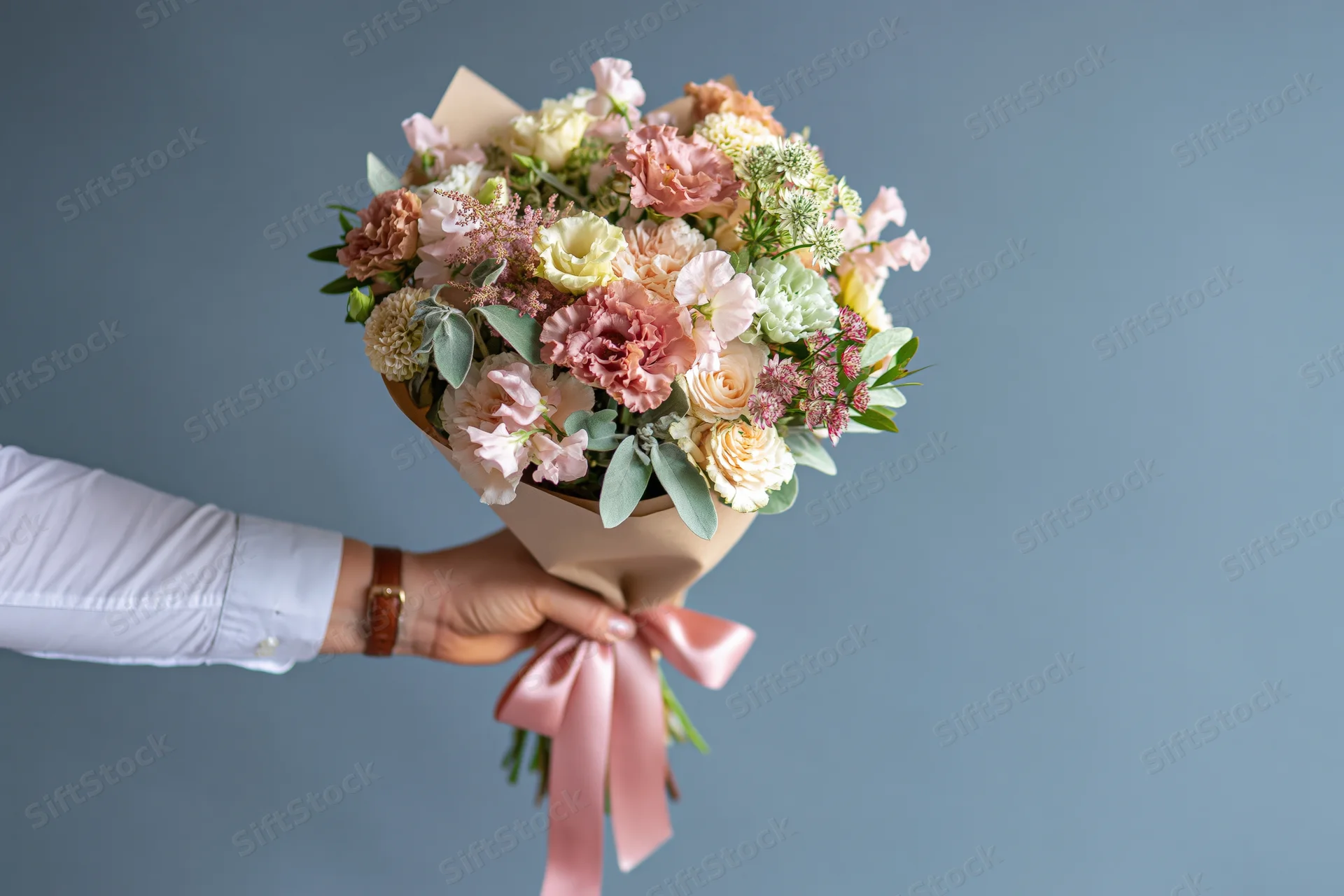 Hand holding a wrapped bouquet of mixed pastel flowers against a plain background