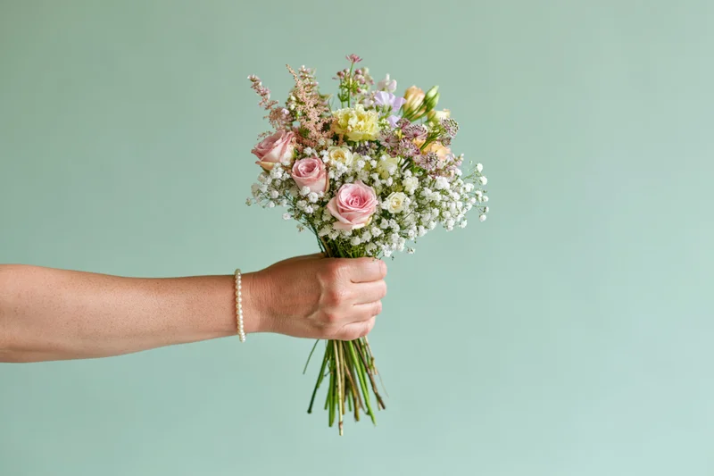 Woman's hand holding a mixed flower bouquet against a mint green background