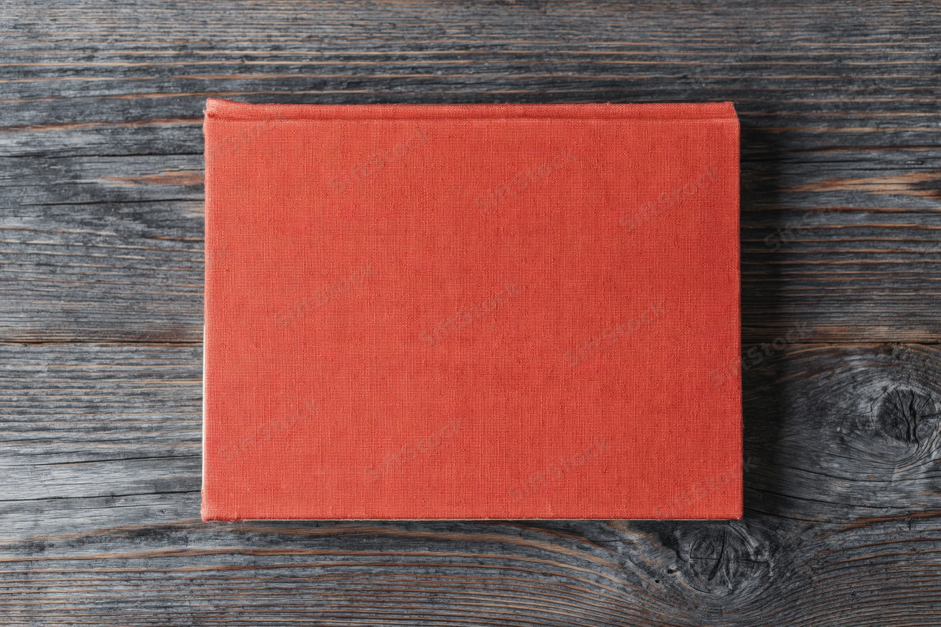 Red hardcover book lying flat on rustic wooden surface